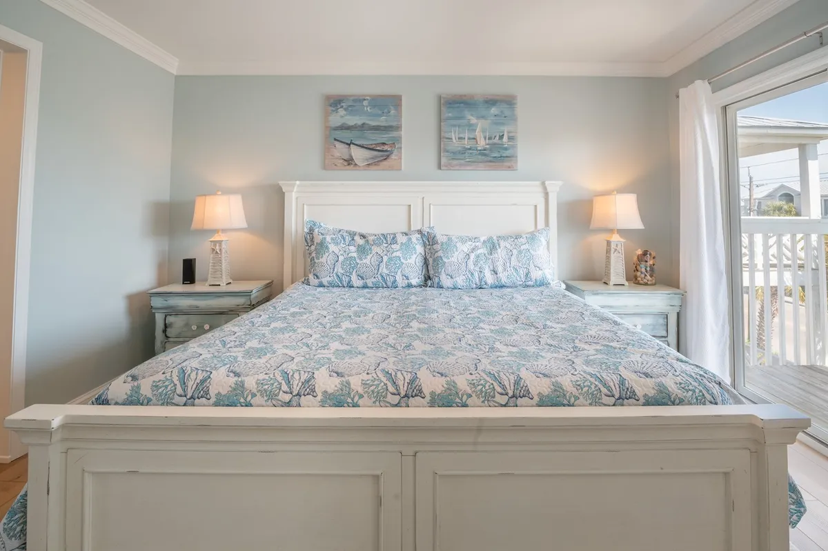 A serene and tranquil bedroom with a comfortable bed, decorative paintings, nightstands, and lamps. The soft lighting and artful decor create an inviting, restful environment perfect for relaxation and enjoying the ambiance after a day by the sea.