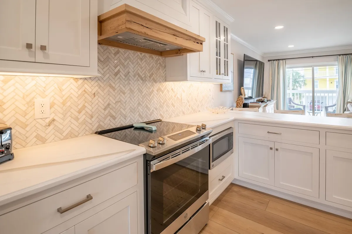 A modern kitchen with a stainless steel stove, wooden hood, and herringbone backsplash. The space feels open and functional, ideal for cooking and gathering.