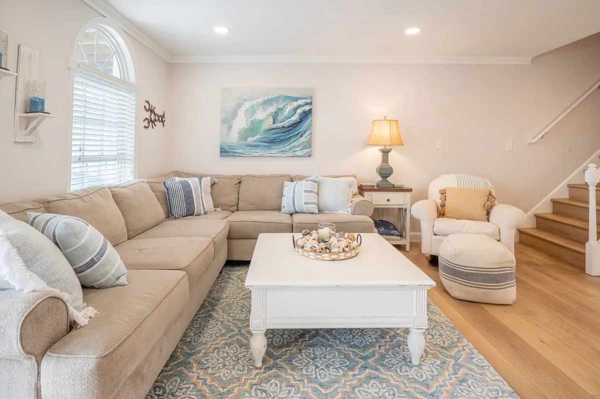 A spacious, comfortable living area with a large sectional sofa, ocean-themed artwork, and a wooden coffee table. The space invites relaxation and group interaction.