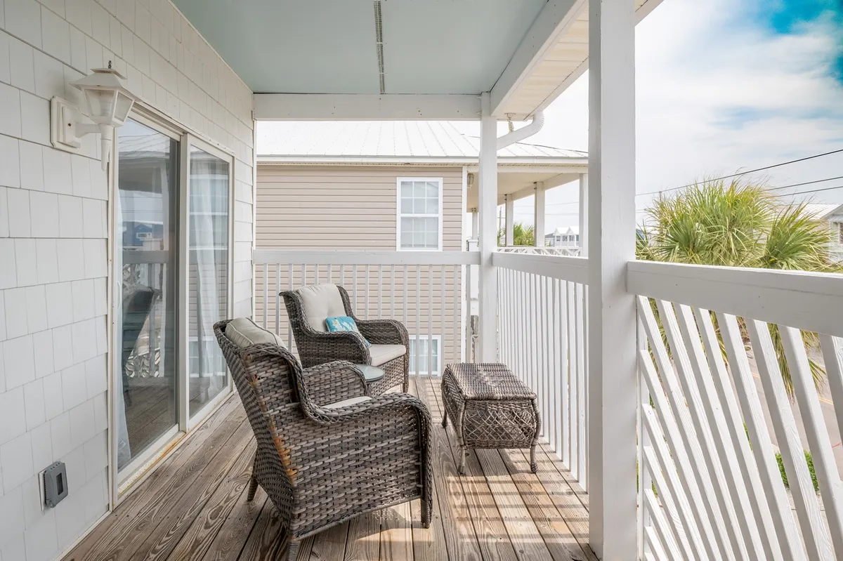 A welcoming outdoor seating area with woven patio chairs and a small table faces an open, unobstructed ocean view. The setting is perfect for relaxing with a drink and watching the sun dip below the horizon, enhanced by the gentle sea breeze.